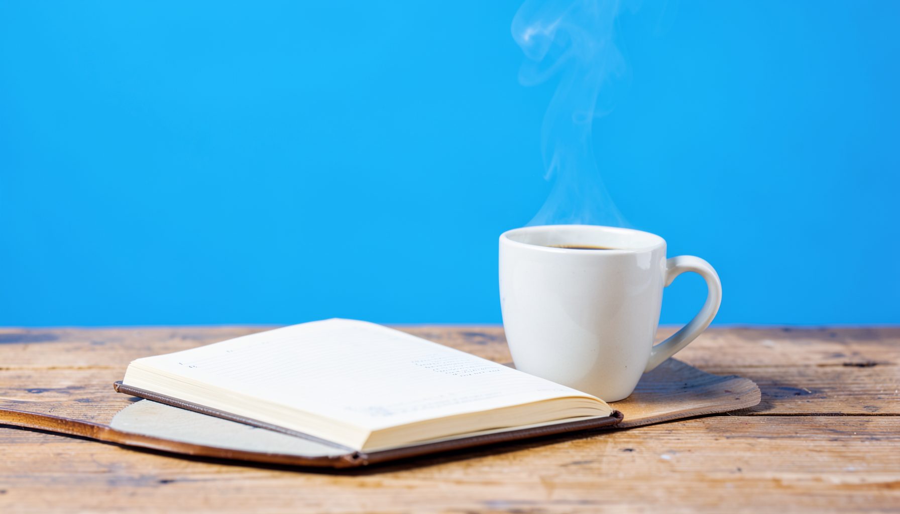 A bright morning scene with a steaming coffee cup on a wooden table beside an open notebook, bathed in soft daylight.